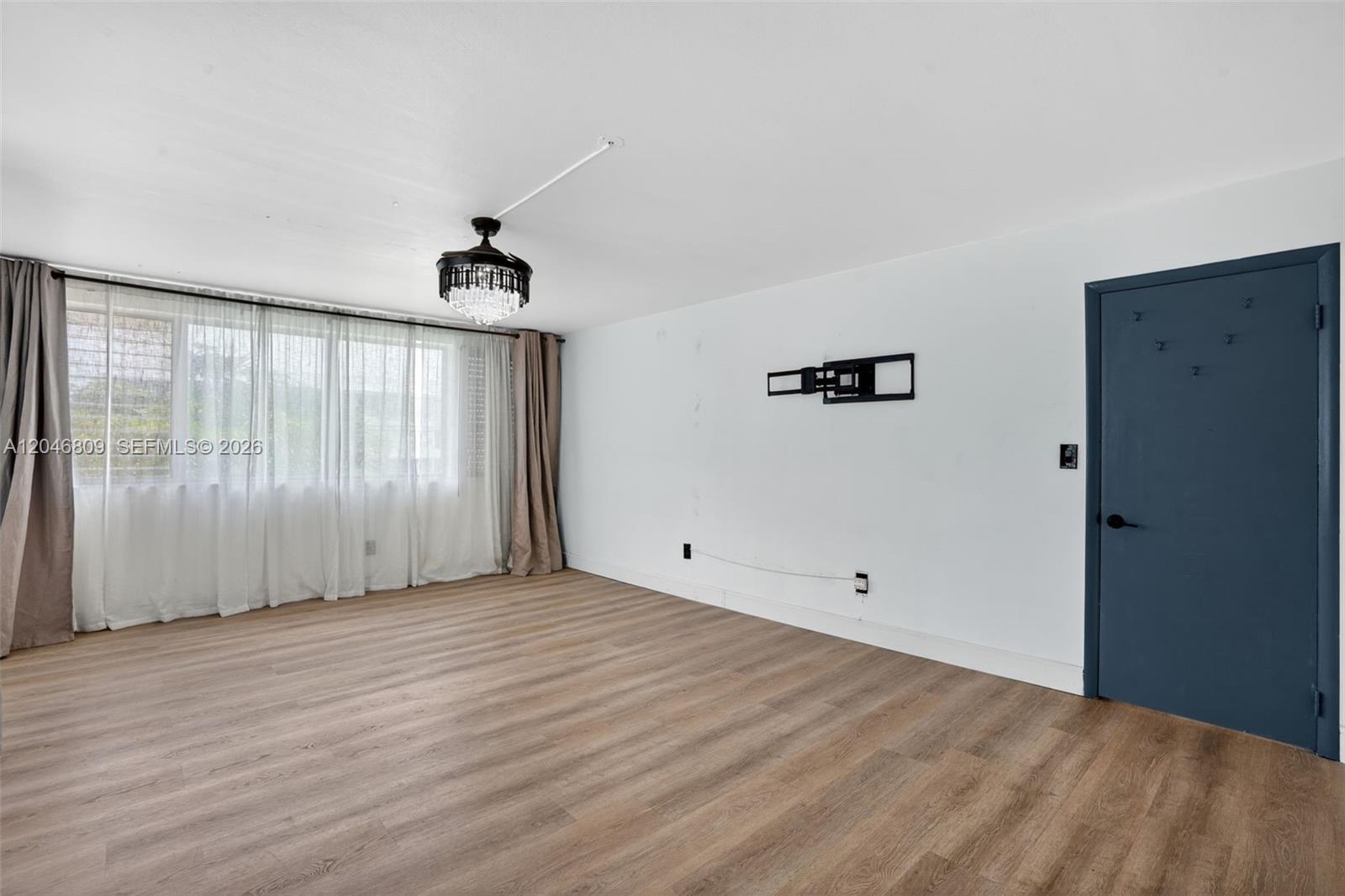 An empty room features wood-look flooring, a crystal ceiling fan, and a wall-mounted television bracket — 10240 Collins Ave # 207, Bal Harbour FL 33154, BAL HARBOUR, FL