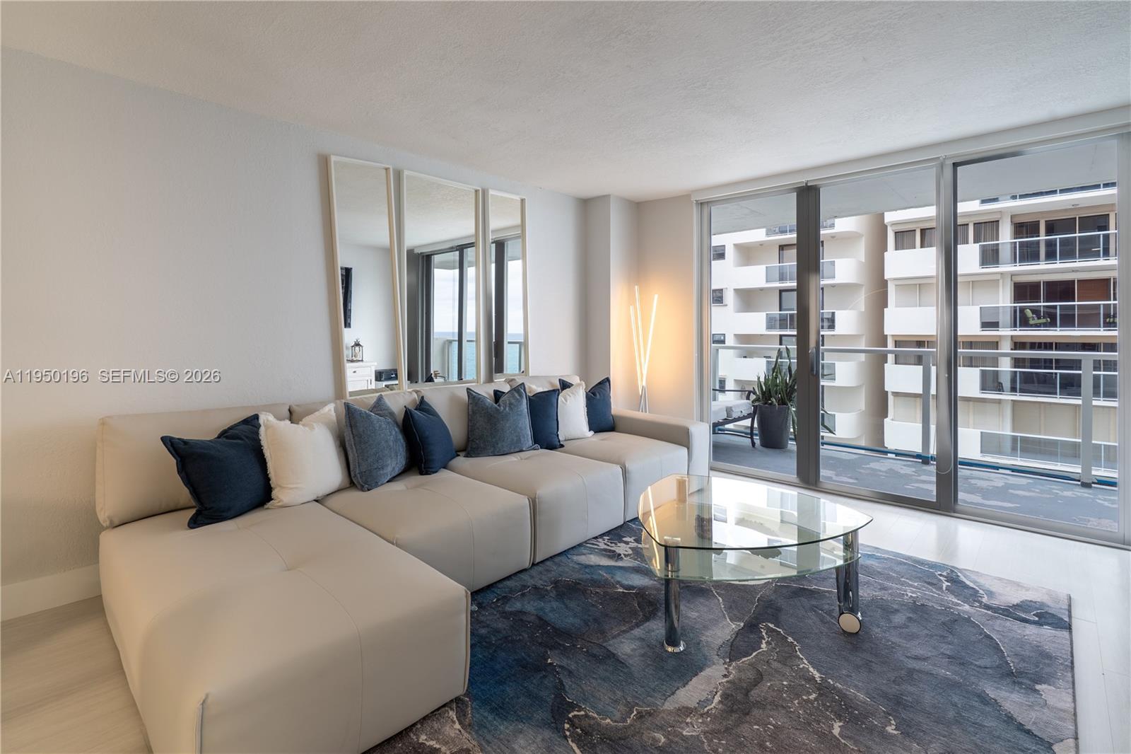 A living room features a light-colored sectional sofa, a glass coffee table, and a balcony — 5701 Collins Ave # 1417, Miami Beach FL 33140, MIAMI BEACH, FL