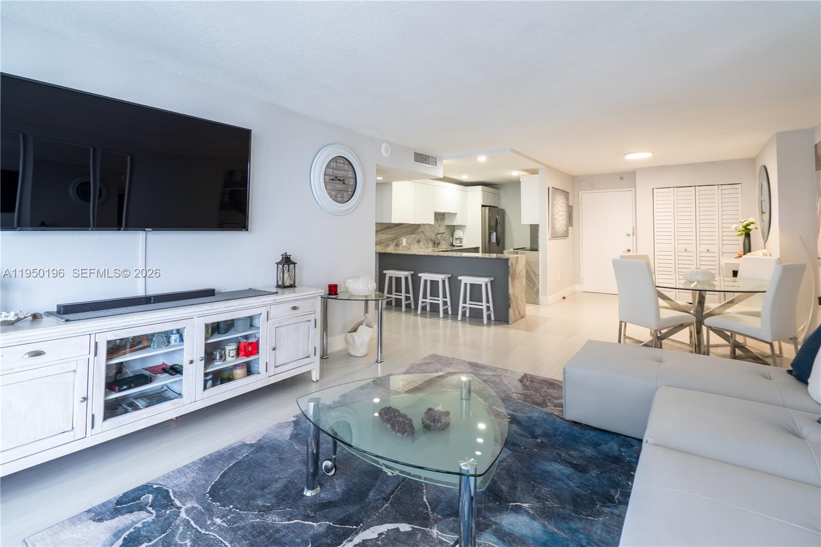 A living room features a white media console, a glass coffee table, and an open kitchen — 5701 Collins Ave # 1417, Miami Beach FL 33140, MIAMI BEACH, FL
