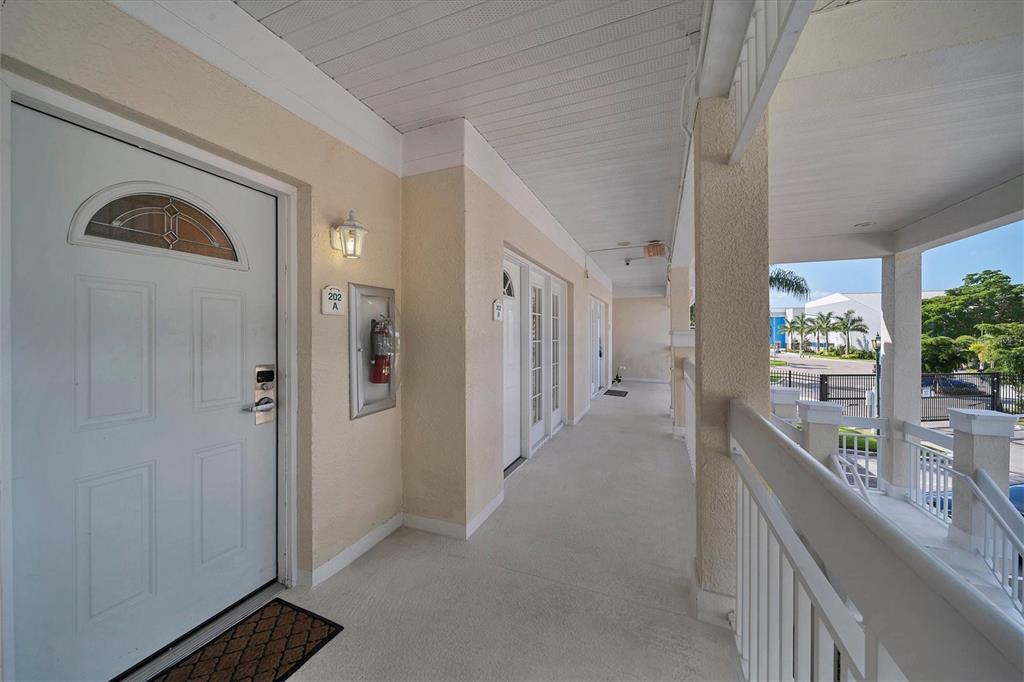 An outdoor covered walkway leads to several white doors with a fire extinguisher nearby — 3401 54TH DRIVE W UNIT 202, BRADENTON, FL