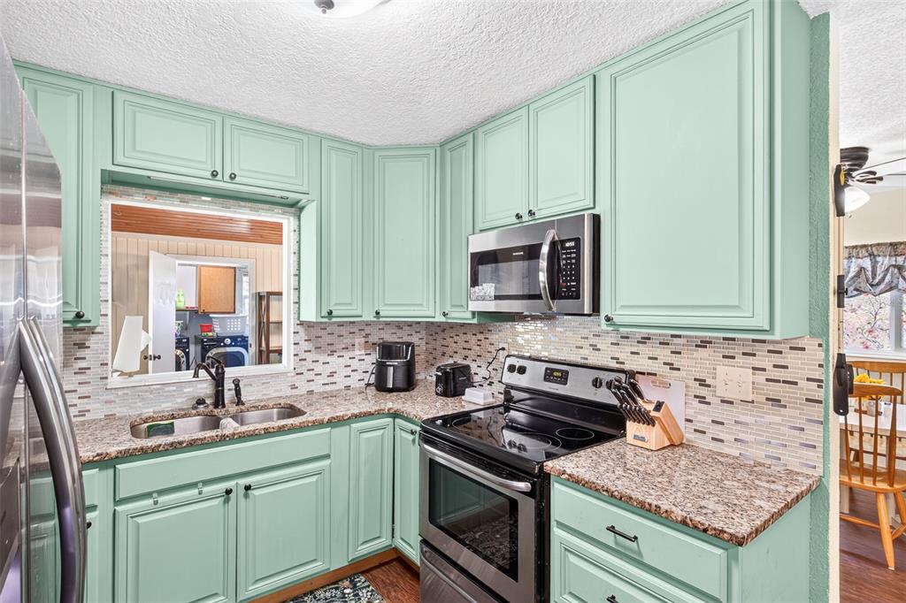 A kitchen features mint green cabinets, granite countertops, stainless steel appliances, and a tiled backsplash — 2021 OLIVER PLACE, WINTER HAVEN, FL