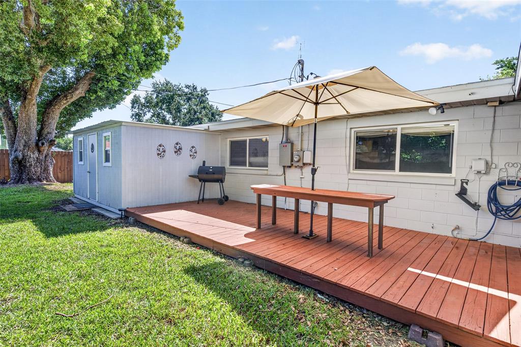 A wooden deck with a patio umbrella and grill sits beside a house and shed — 2021 OLIVER PLACE, WINTER HAVEN, FL