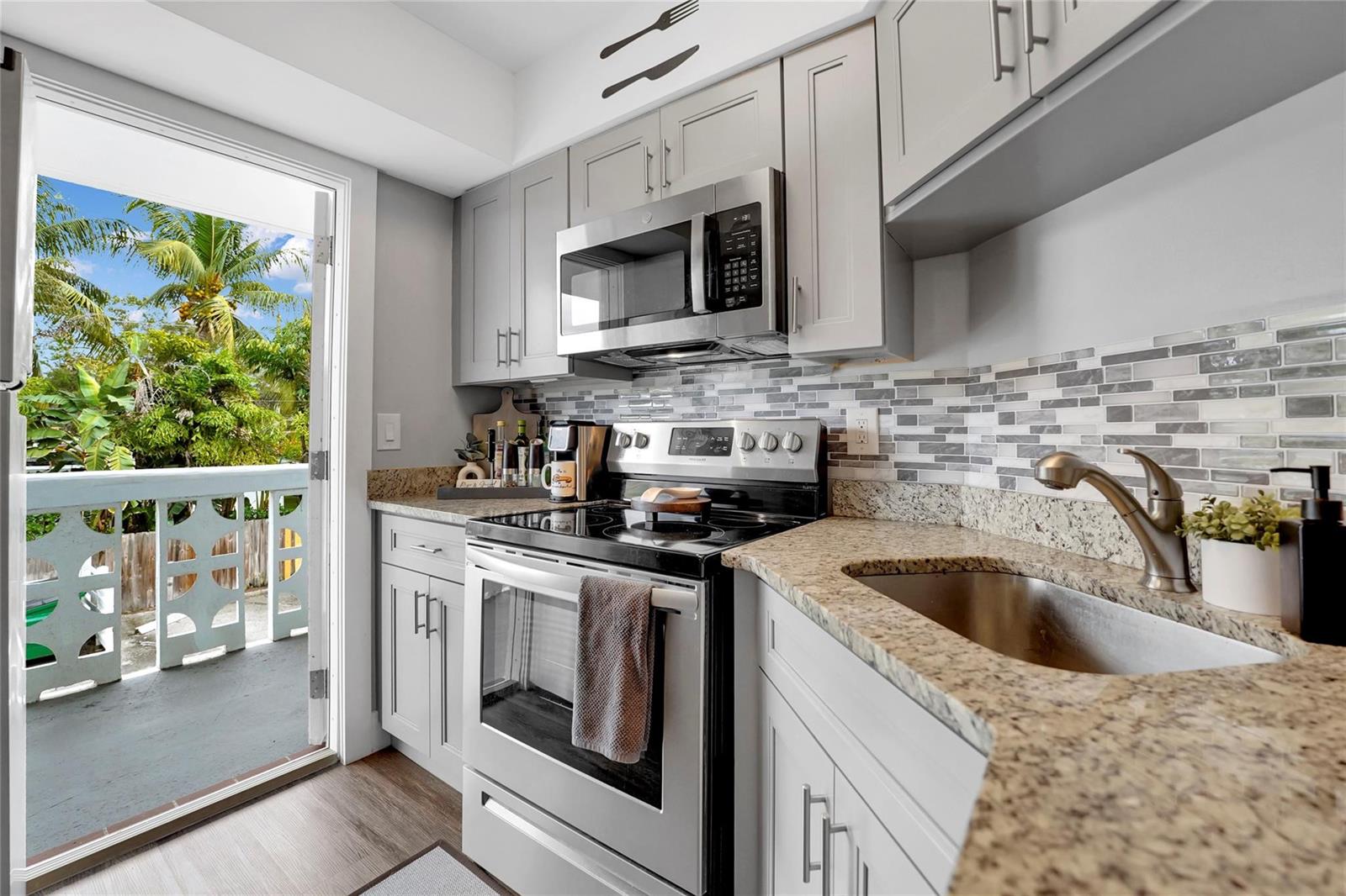 A kitchen features gray cabinets, granite countertops, stainless steel appliances, and a balcony door — 2161 NE 42nd Court # 215, Lighthouse Point FL 33064, LIGHTHOUSE POINT, FL