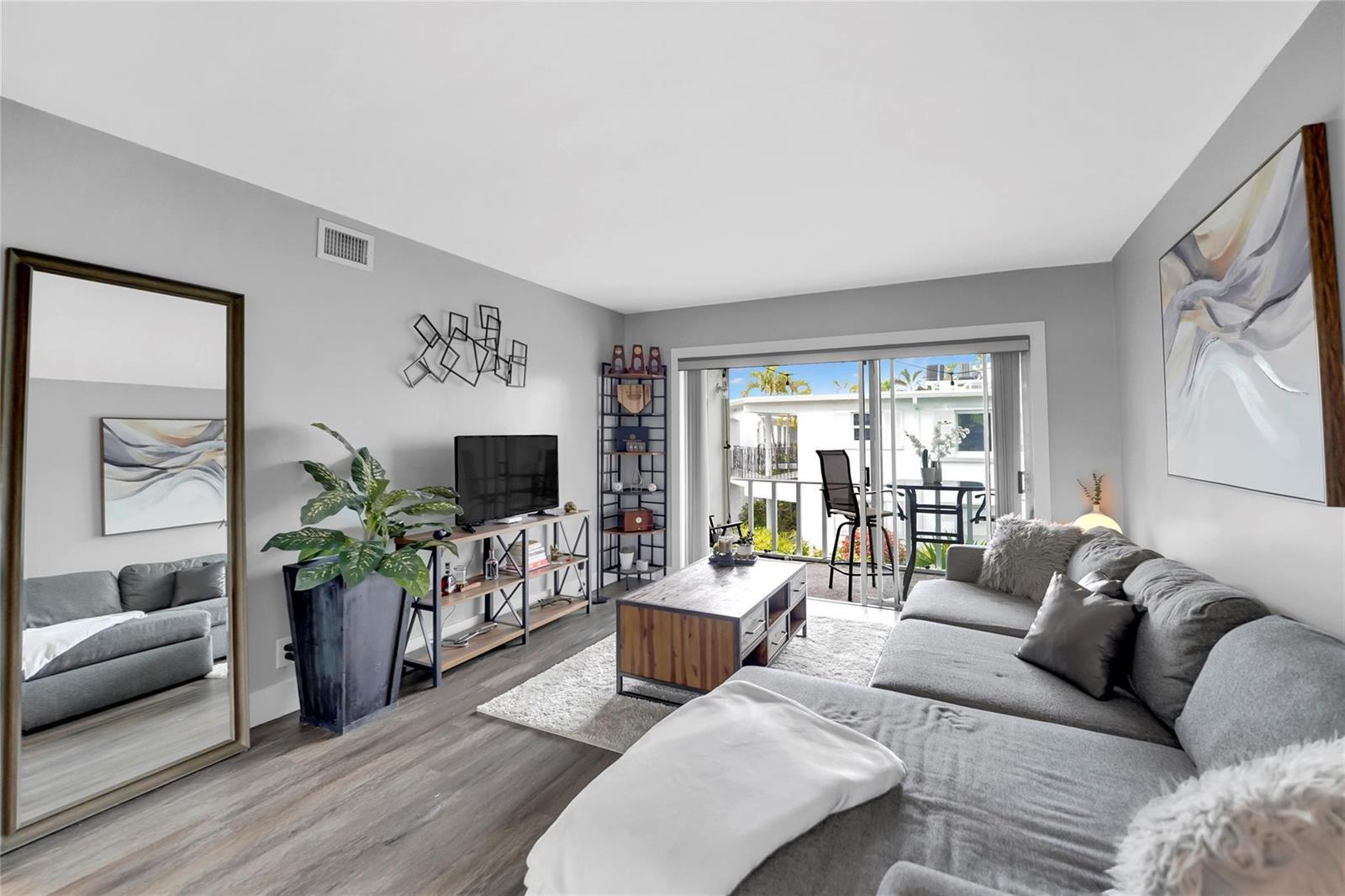 A living room features gray walls, wood-look flooring, a sectional sofa, and a sliding glass door — 2161 NE 42nd Court # 215, Lighthouse Point FL 33064, LIGHTHOUSE POINT, FL