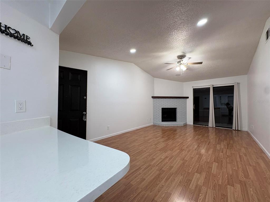 A living room features wood-look flooring, a white brick fireplace, and a black entry door — 1724 FOXHALL CIRCLE UNIT 1724, KISSIMMEE, FL
