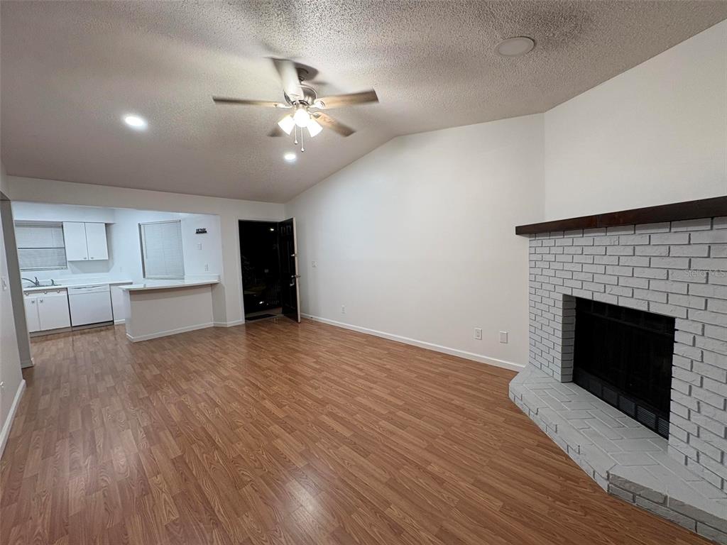 A living room with wood-look flooring, a white brick fireplace, and an adjacent kitchen area — 1724 FOXHALL CIRCLE UNIT 1724, KISSIMMEE, FL