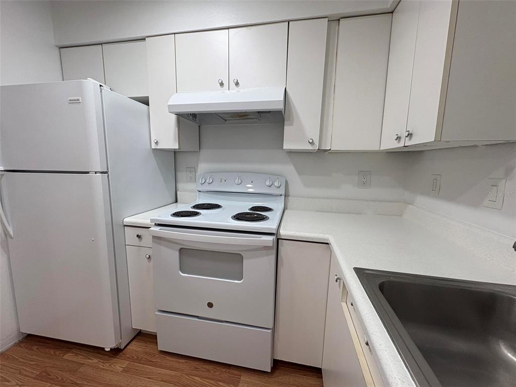A kitchen features white appliances, white cabinetry, and light-colored countertops over wood-look flooring — 1724 FOXHALL CIRCLE UNIT 1724, KISSIMMEE, FL