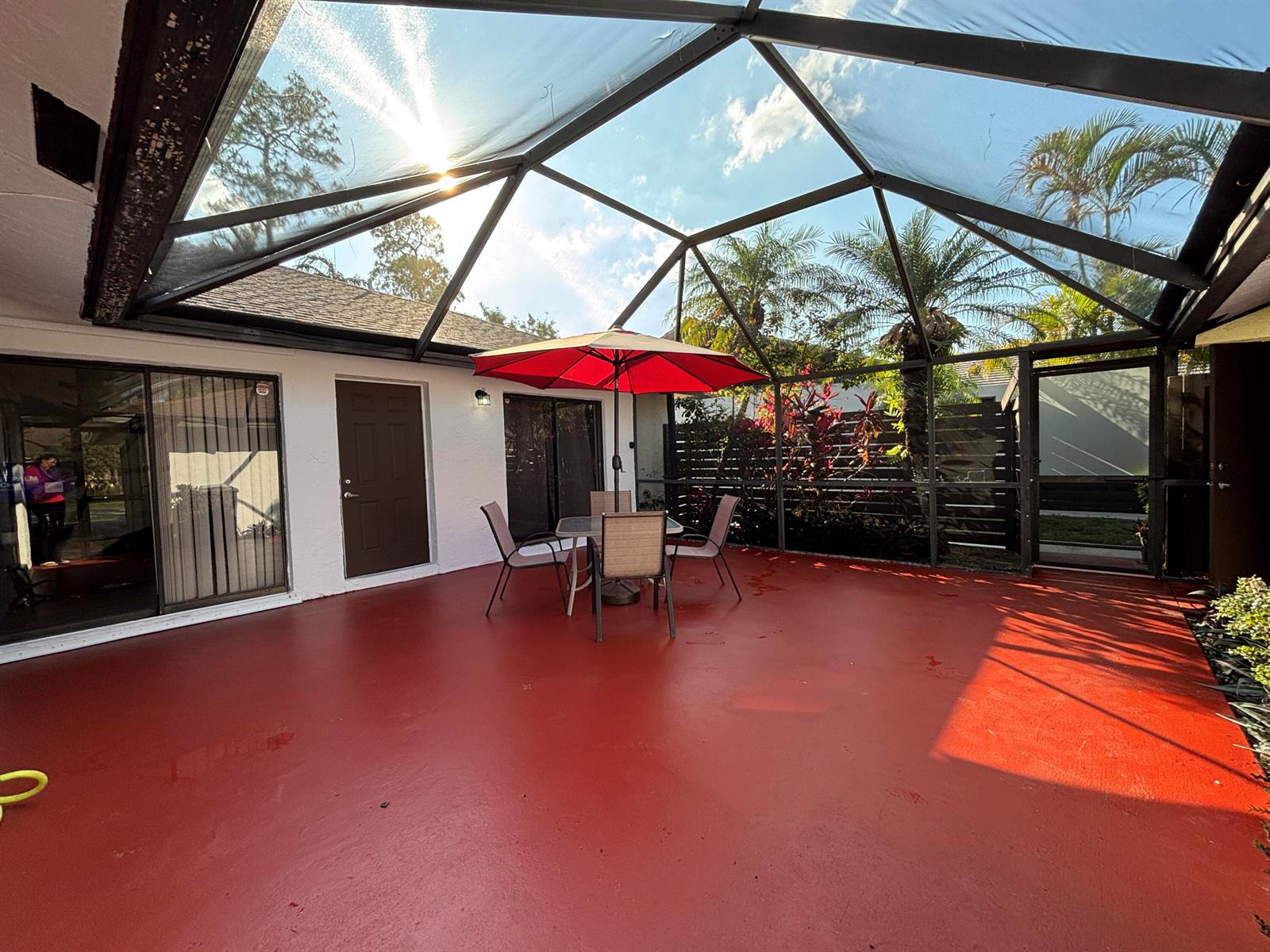 A screened-in patio features a red concrete floor, outdoor dining furniture, and a red umbrella — 1289 Periwinkle Place, Wellington FL 33414, WELLINGTON, FL