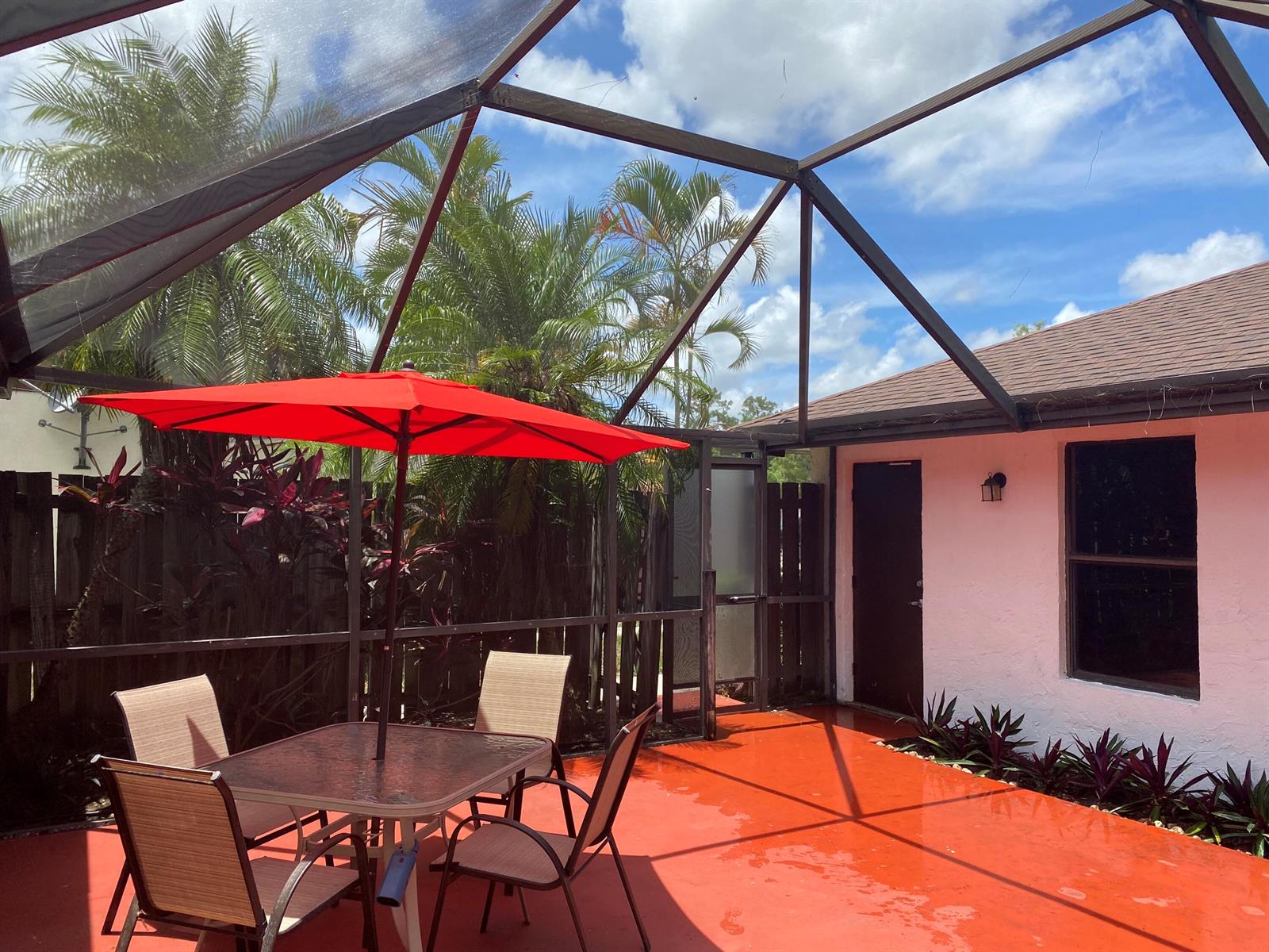 A screened-in patio features a red concrete floor, a dining set, and a red umbrella — 1289 Periwinkle Place, Wellington FL 33414, WELLINGTON, FL