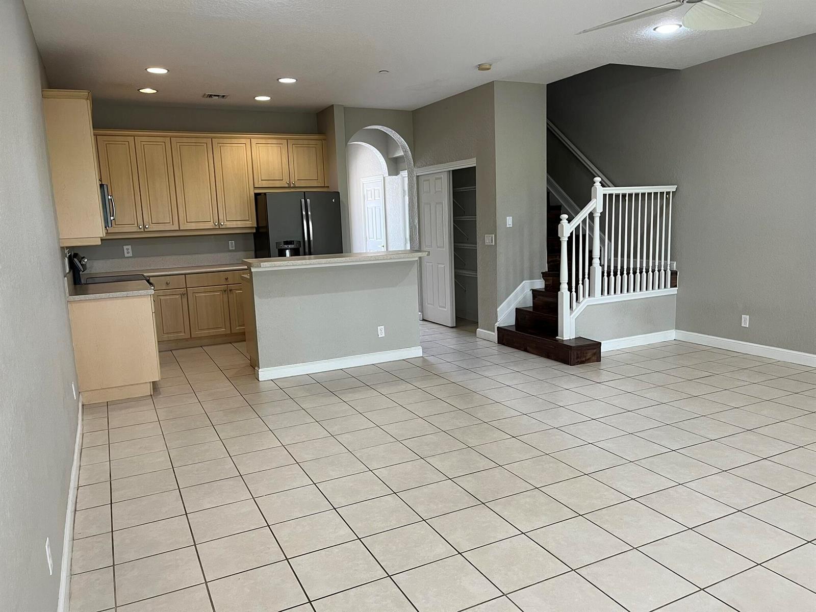 A kitchen with light wood cabinets and a breakfast bar opens to a tiled living area — 404 SE Bloxham Way, Stuart FL 34997, STUART, FL
