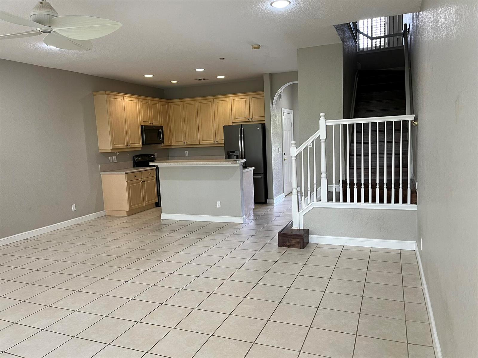 An open-concept kitchen with light wood cabinets and tile flooring sits beside a staircase — 404 SE Bloxham Way, Stuart FL 34997, STUART, FL