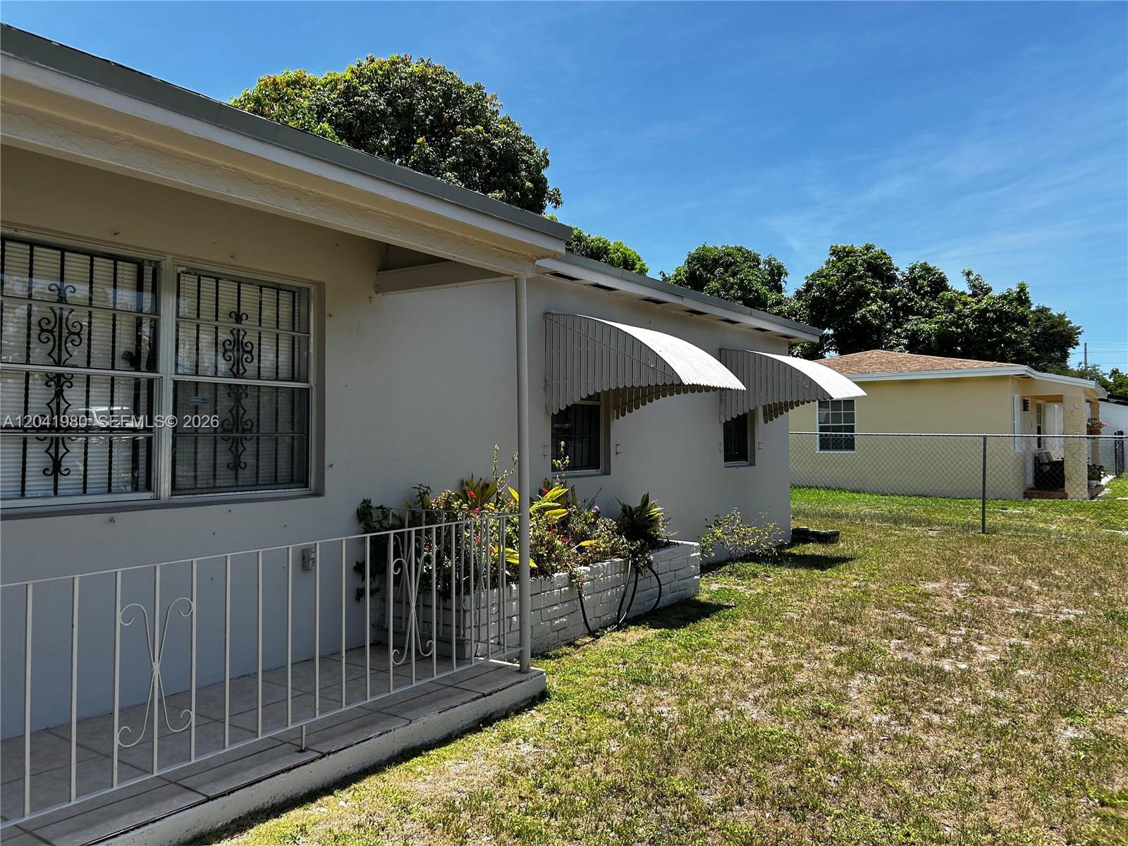 The exterior of a light-colored house features a front porch, metal awnings, and security bars — 295 NW 189th Ter, Miami Gardens FL 33169, MIAMI GARDENS, FL