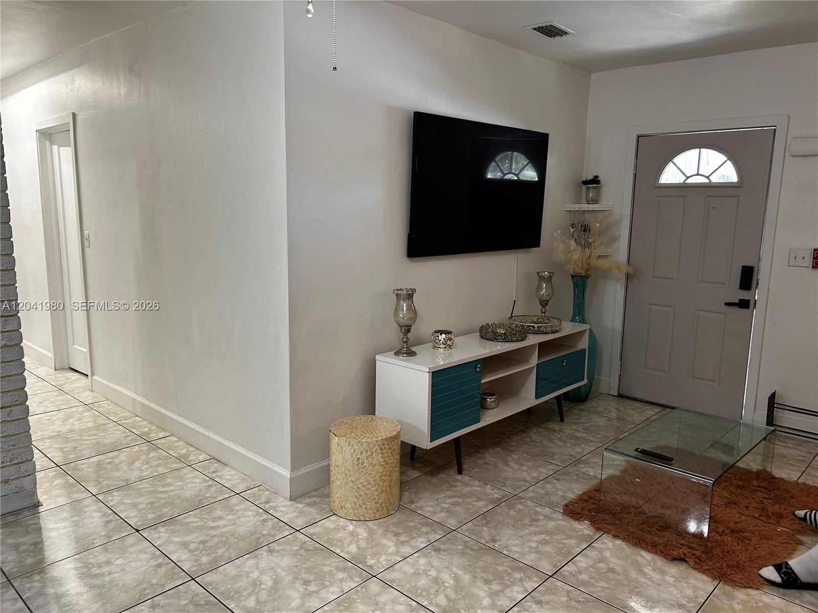 A living room features a wall-mounted television, a white and teal media console, and tile flooring — 295 NW 189th Ter, Miami Gardens FL 33169, MIAMI GARDENS, FL