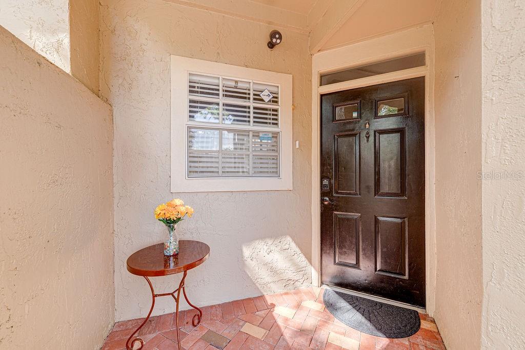 A small covered entryway features a brick floor, a dark front door, and a side table — 1545 FARRINDON CIRCLE UNIT 1545, LAKE MARY, FL