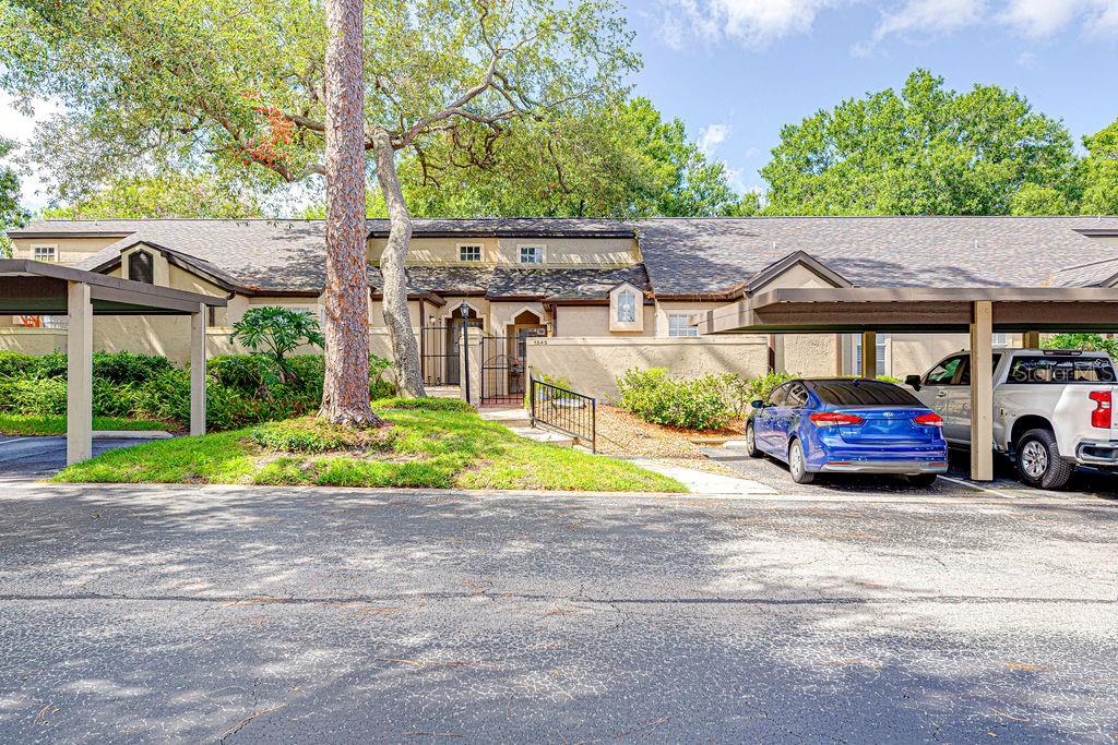 A tan townhome exterior features a covered parking area, a small courtyard, and mature trees — 1545 FARRINDON CIRCLE UNIT 1545, LAKE MARY, FL