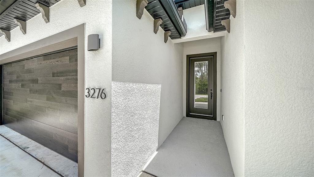 A modern home exterior features a wood-paneled garage door, white stucco walls, and a glass-paneled door — 3276 CHIPLEY AVENUE, NORTH PORT, FL