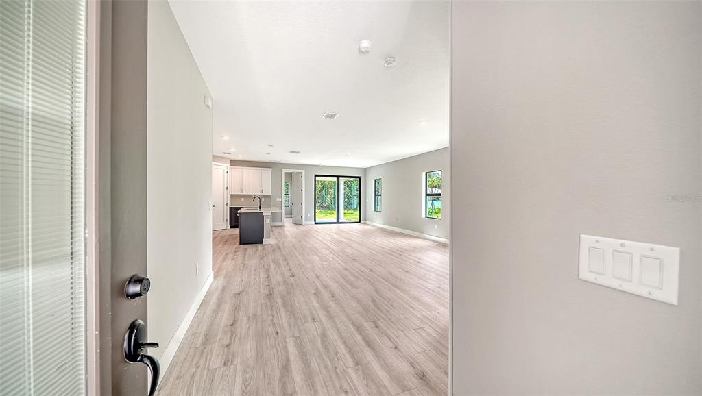 An open-concept living area with light wood-look flooring, a kitchen island, and sliding glass doors — 3276 CHIPLEY AVENUE, NORTH PORT, FL