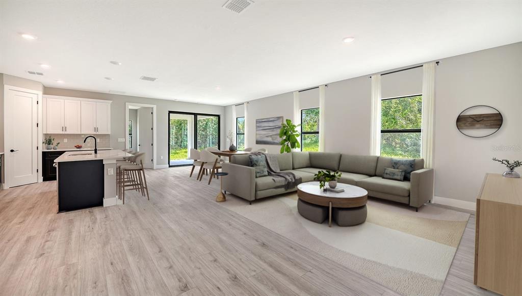 This open-concept living room features a kitchen island, a sectional sofa, and large windows — 3276 CHIPLEY AVENUE, NORTH PORT, FL