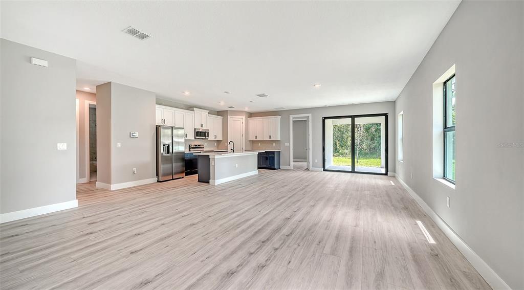 An open-concept kitchen and living area features light wood-look flooring, white cabinetry, and sliding doors — 3276 CHIPLEY AVENUE, NORTH PORT, FL