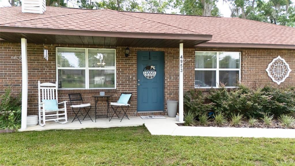 A brick house exterior features a blue front door, a porch with seating, and landscaping — 4953 SE 33RD TERRACE, OCALA, FL
