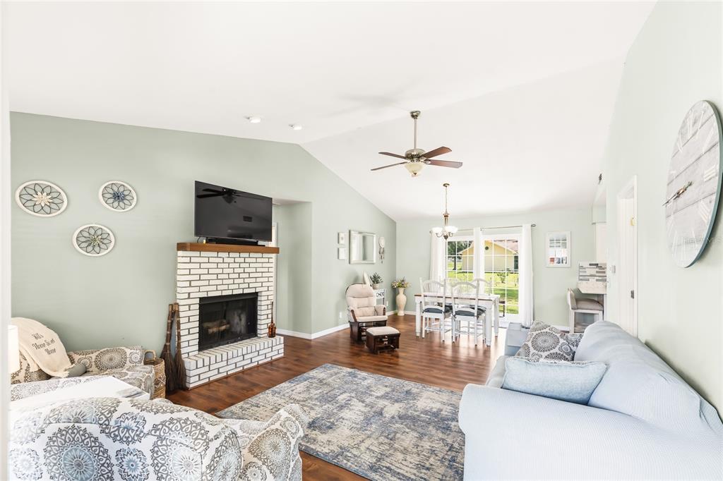 A living room with a white brick fireplace, vaulted ceilings, and a dining area beyond — 4953 SE 33RD TERRACE, OCALA, FL