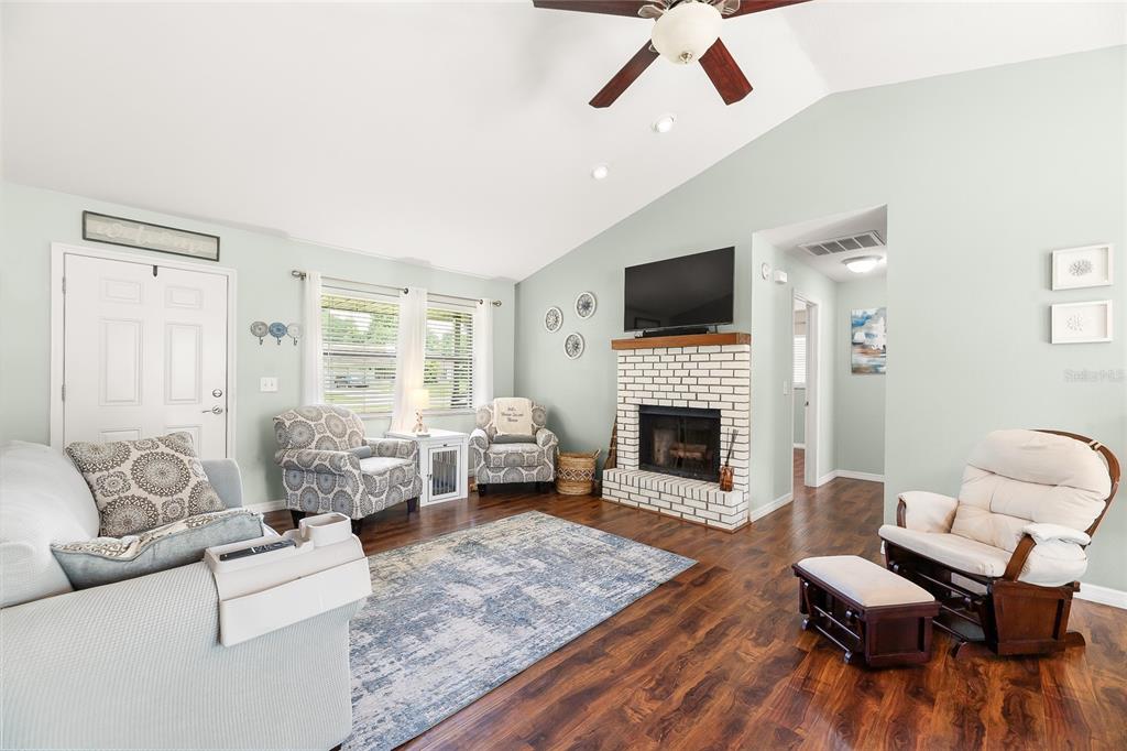 A living room features a white brick fireplace, vaulted ceilings, and wood-look flooring — 4953 SE 33RD TERRACE, OCALA, FL