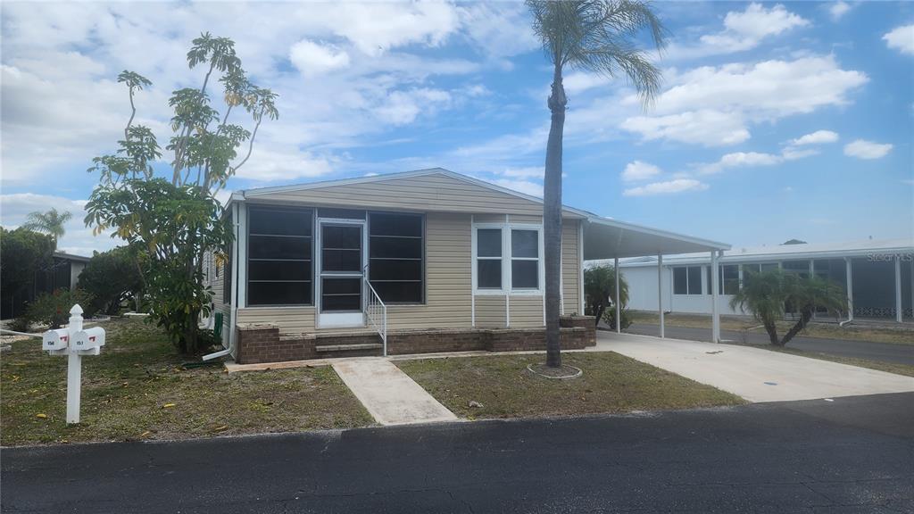 A single-story mobile home with tan siding, a screened-in porch, and an attached carport — 157 N FIJI CIRCLE, ENGLEWOOD, FL