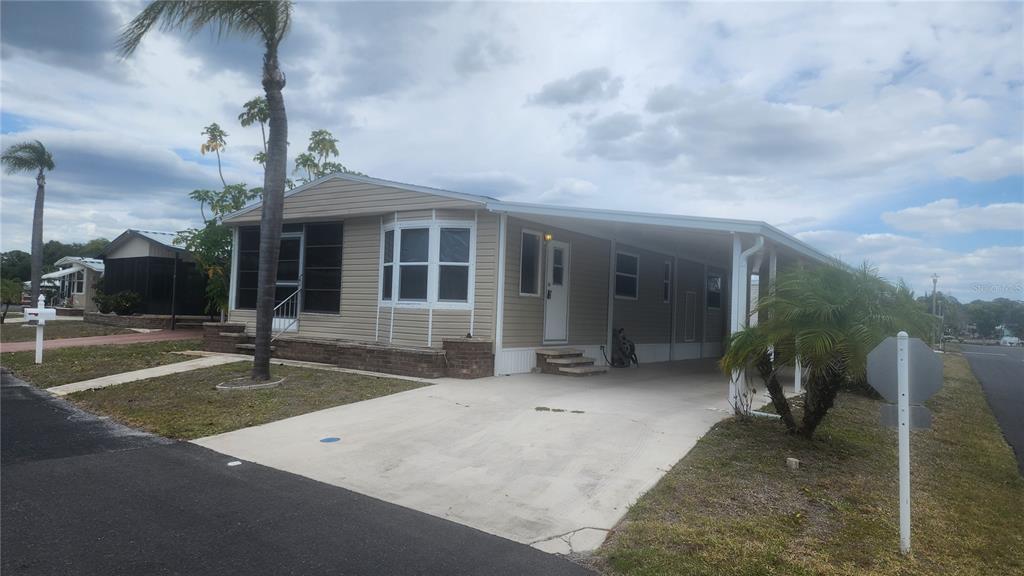 A tan mobile home features a screened porch, a carport, and palm trees — 157 N FIJI CIRCLE, ENGLEWOOD, FL