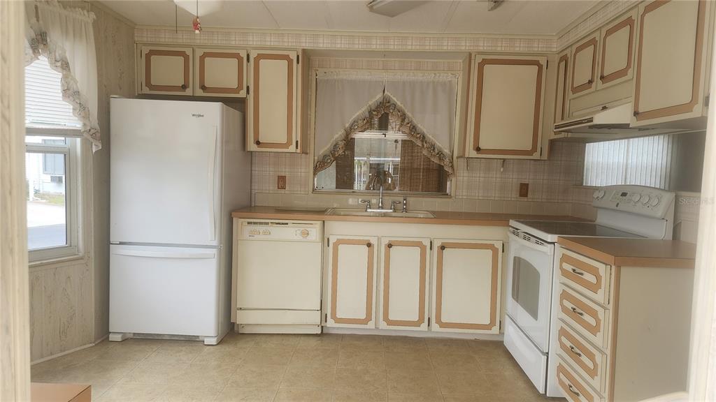 A kitchen with white appliances, light-colored cabinets with brown trim, and a window above the sink — 157 N FIJI CIRCLE, ENGLEWOOD, FL