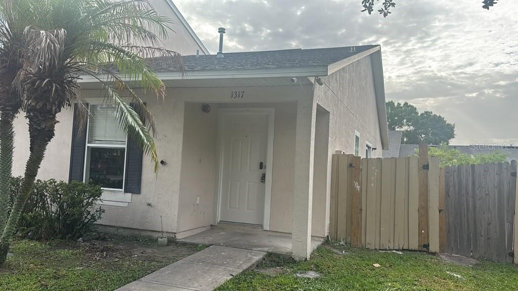A single-story house exterior features a white front door, a palm tree, and wooden fencing — 1317 FETTLER WAY, WINTER GARDEN, FL