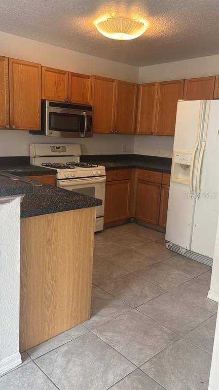 A kitchen features wood cabinets, dark countertops, a white stove, and a white refrigerator — 1317 FETTLER WAY, WINTER GARDEN, FL