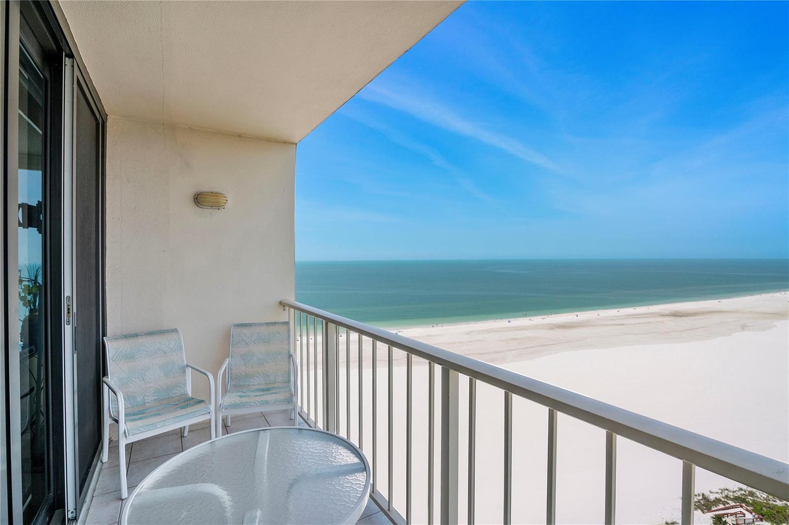 A balcony with two chairs and a glass table overlooks a sandy beach and ocean — 58 N Collier Boulevard # 2108, Marco Island FL 34145, MARCO ISLAND, FL