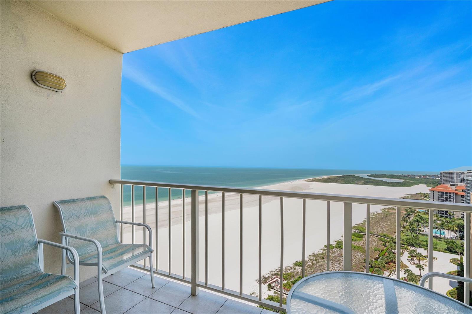 A balcony with two chairs and a glass table overlooks a beach and ocean — 58 N Collier Boulevard # 2108, Marco Island FL 34145, MARCO ISLAND, FL