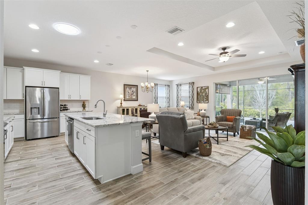 An open-concept kitchen and living area features white cabinetry, granite countertops, and wood-look tile flooring — 1157 AVERY MEADOWS WAY, DELAND, FL