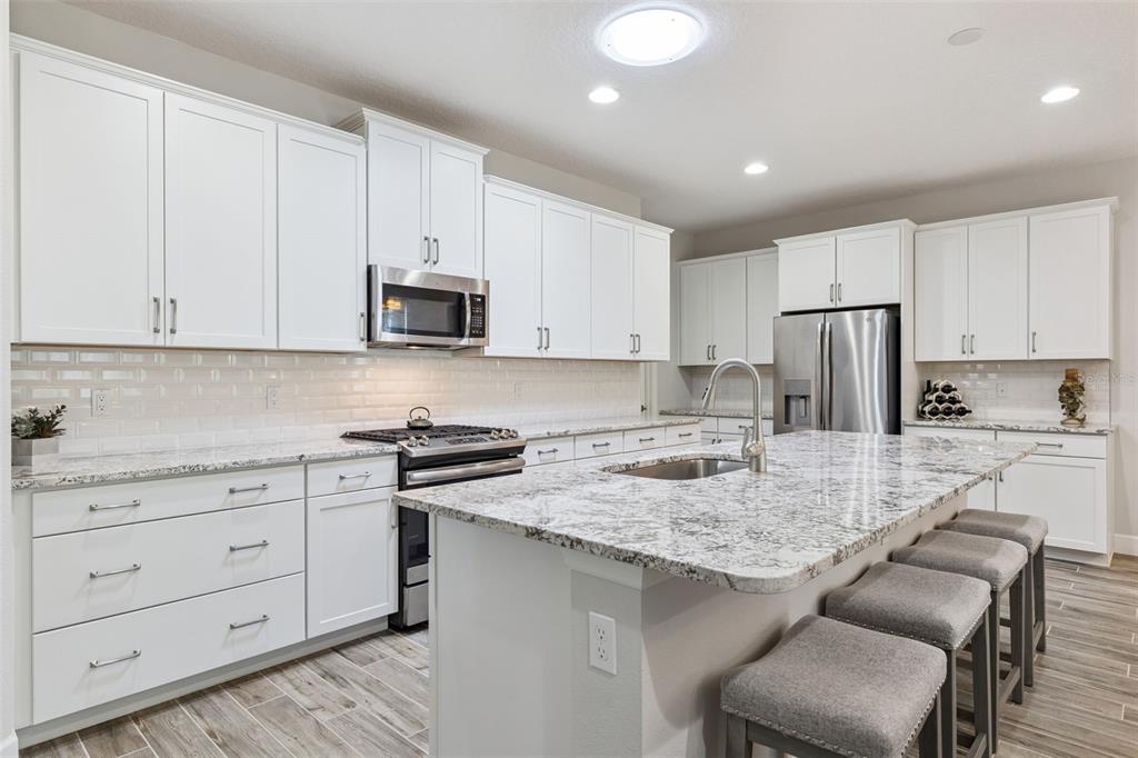 A modern kitchen features white cabinets, granite countertops, a large island, and stainless steel appliances — 1157 AVERY MEADOWS WAY, DELAND, FL