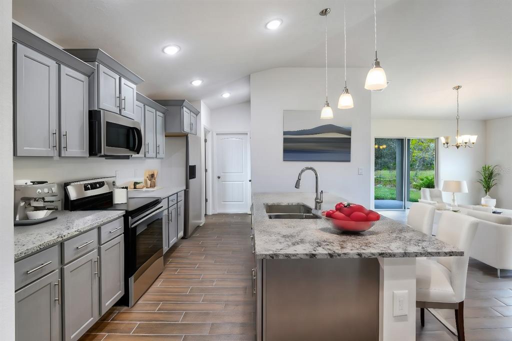A kitchen with grey cabinets, granite countertops, and an island overlooking a living area — 179 AURELIA COURT, KISSIMMEE, FL