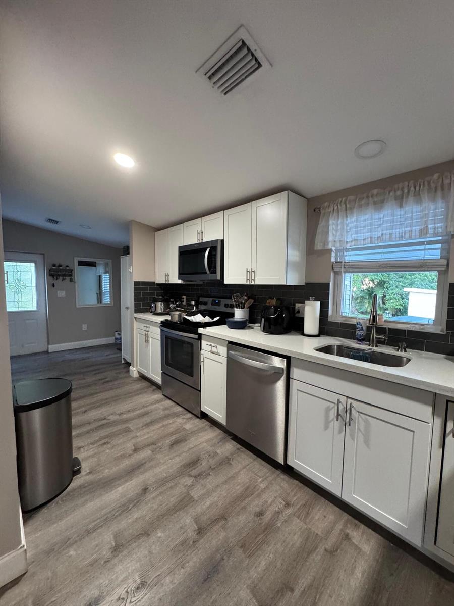 A kitchen features white cabinets, stainless steel appliances, dark tile backsplash, and wood-look flooring — 3899 Redman Parkway # 143, Boynton Beach FL 33436, BOYNTON BEACH, FL