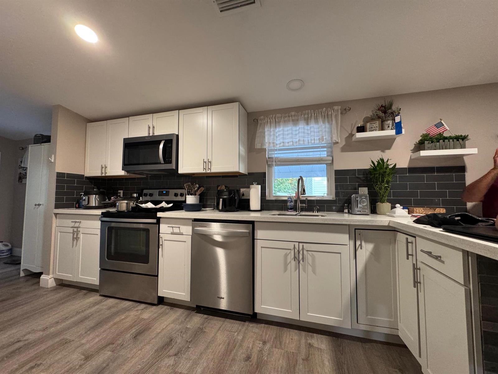 A kitchen features white cabinets, stainless steel appliances, dark subway tile backsplash, and wood-look flooring — 3899 Redman Parkway # 143, Boynton Beach FL 33436, BOYNTON BEACH, FL