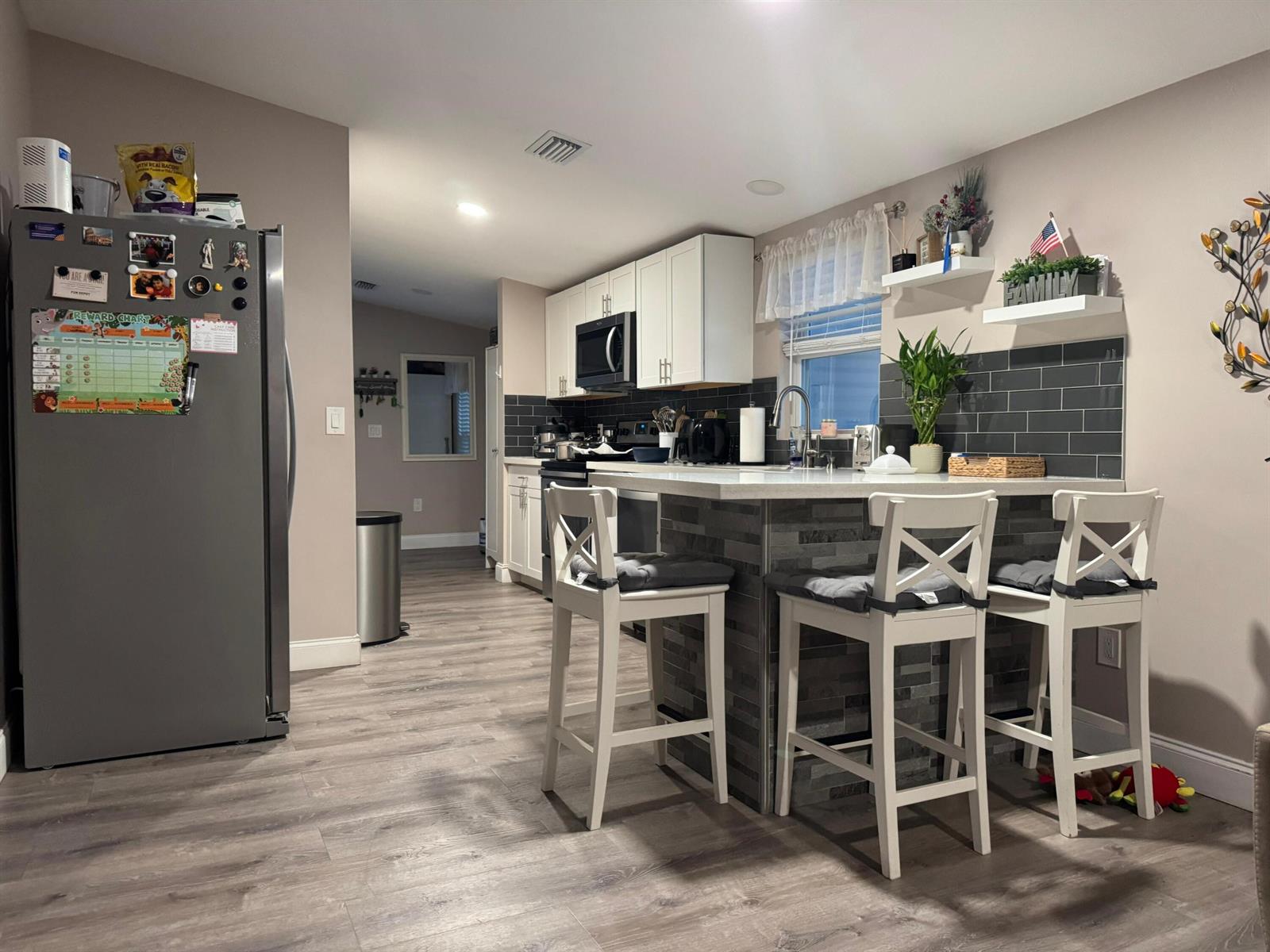 A kitchen features white cabinets, a gray tiled backsplash, a breakfast island, and stainless appliances — 3899 Redman Parkway # 143, Boynton Beach FL 33436, BOYNTON BEACH, FL