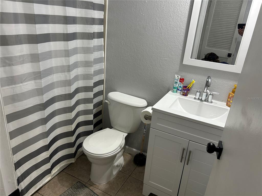 A bathroom features a white vanity, a toilet, and a gray and white striped shower curtain — 6301 58TH STREET N UNIT 506, PINELLAS PARK, FL