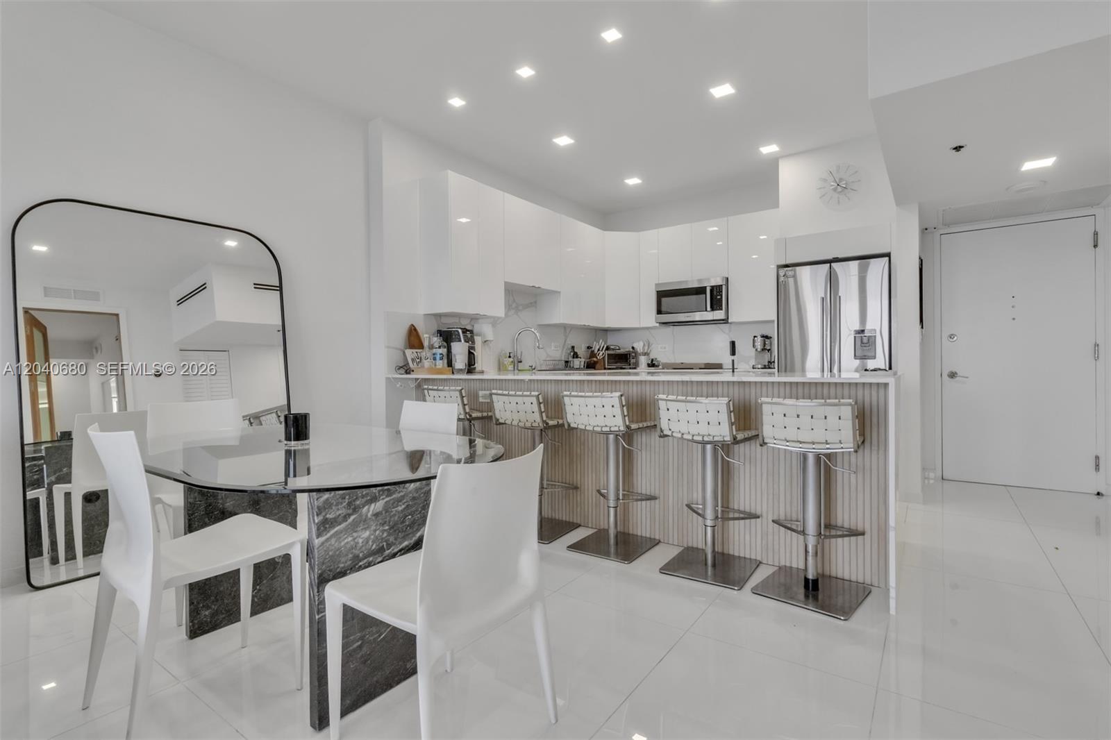 A modern kitchen features white cabinetry, a marble-topped island with bar stools, and a dining area — 5701 Collins Ave, Miami Beach FL 33140, MIAMI BEACH, FL