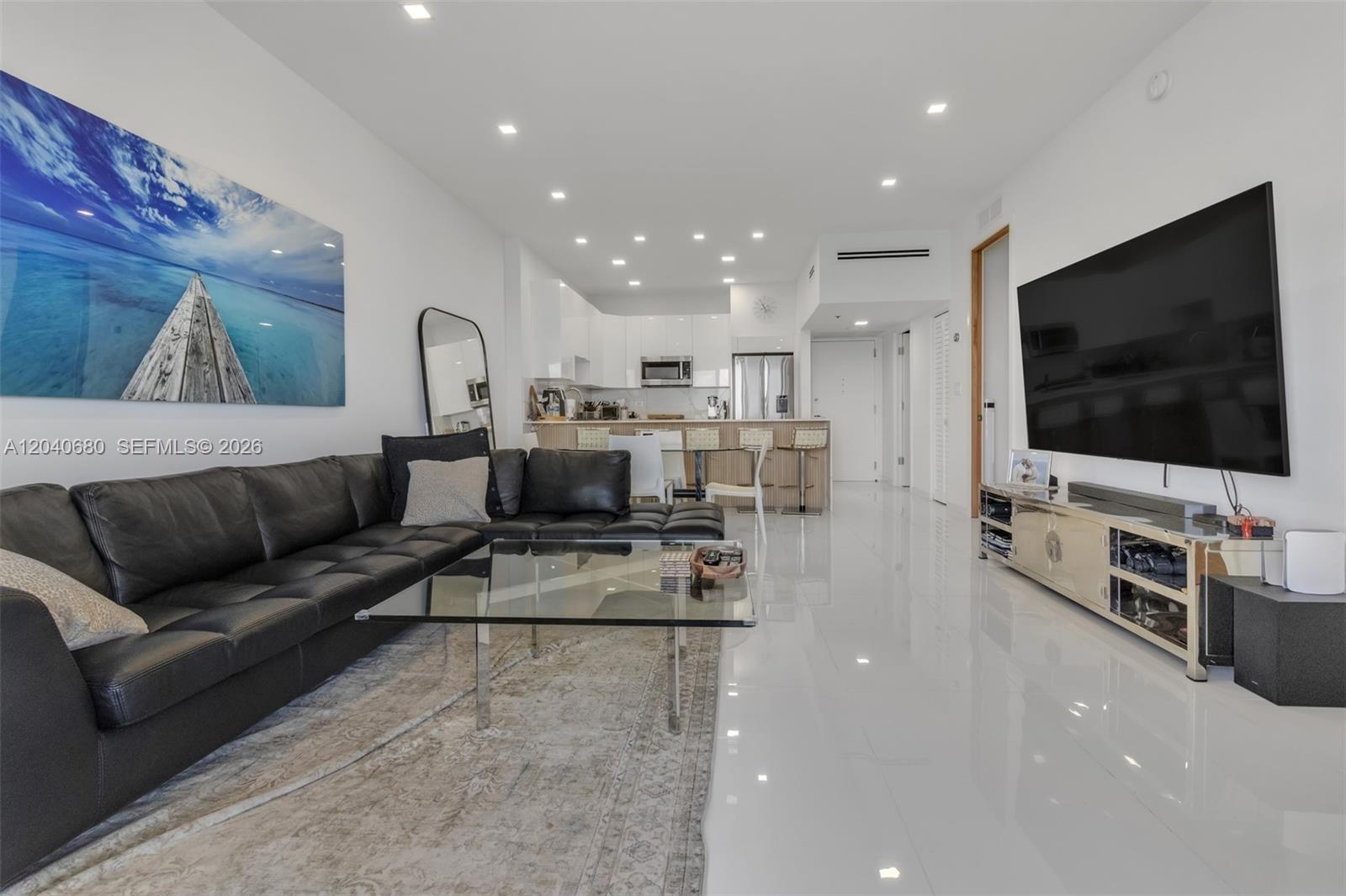 A modern living room features a black sectional sofa, glass coffee table, and white tile floors — 5701 Collins Ave, Miami Beach FL 33140, MIAMI BEACH, FL