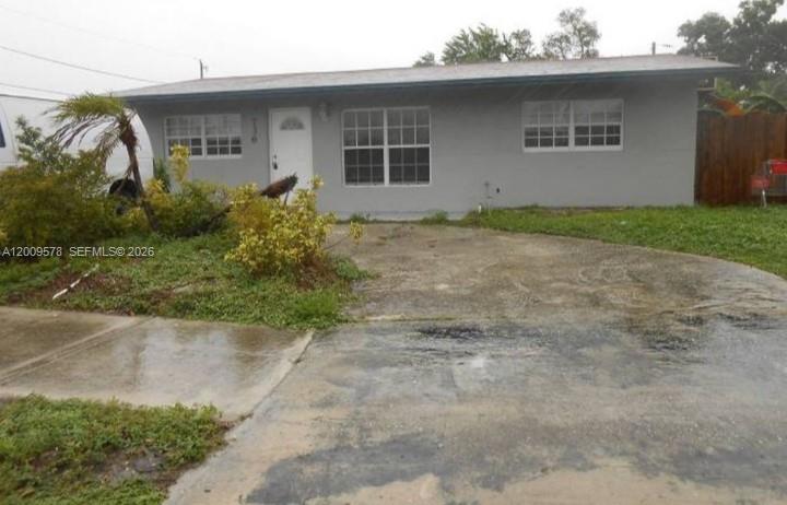 A single-story gray house with a concrete driveway and a front yard — DEERFIELD BEACH, FL