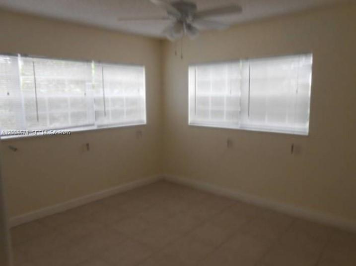 An empty room features light-colored tile flooring, white walls, and two windows with blinds — DEERFIELD BEACH, FL