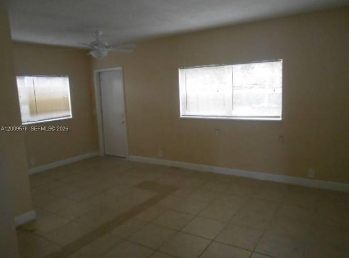 An empty room features beige tile flooring, a ceiling fan, and two windows — DEERFIELD BEACH, FL
