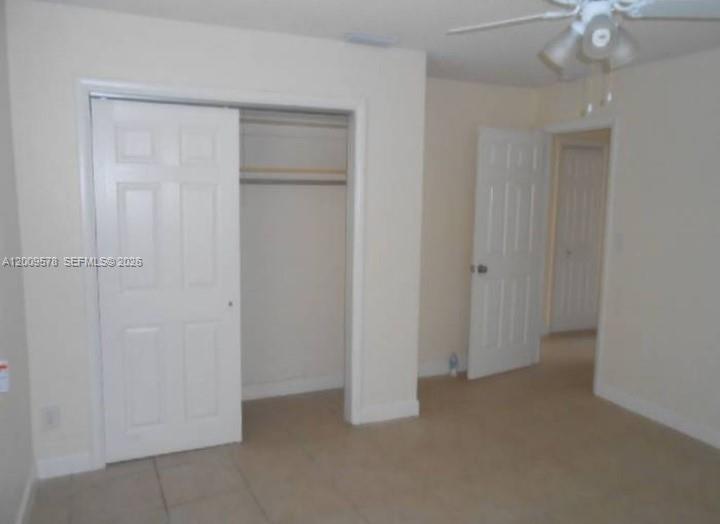 A bedroom features beige walls, tile flooring, a sliding closet door, and a white interior door — DEERFIELD BEACH, FL