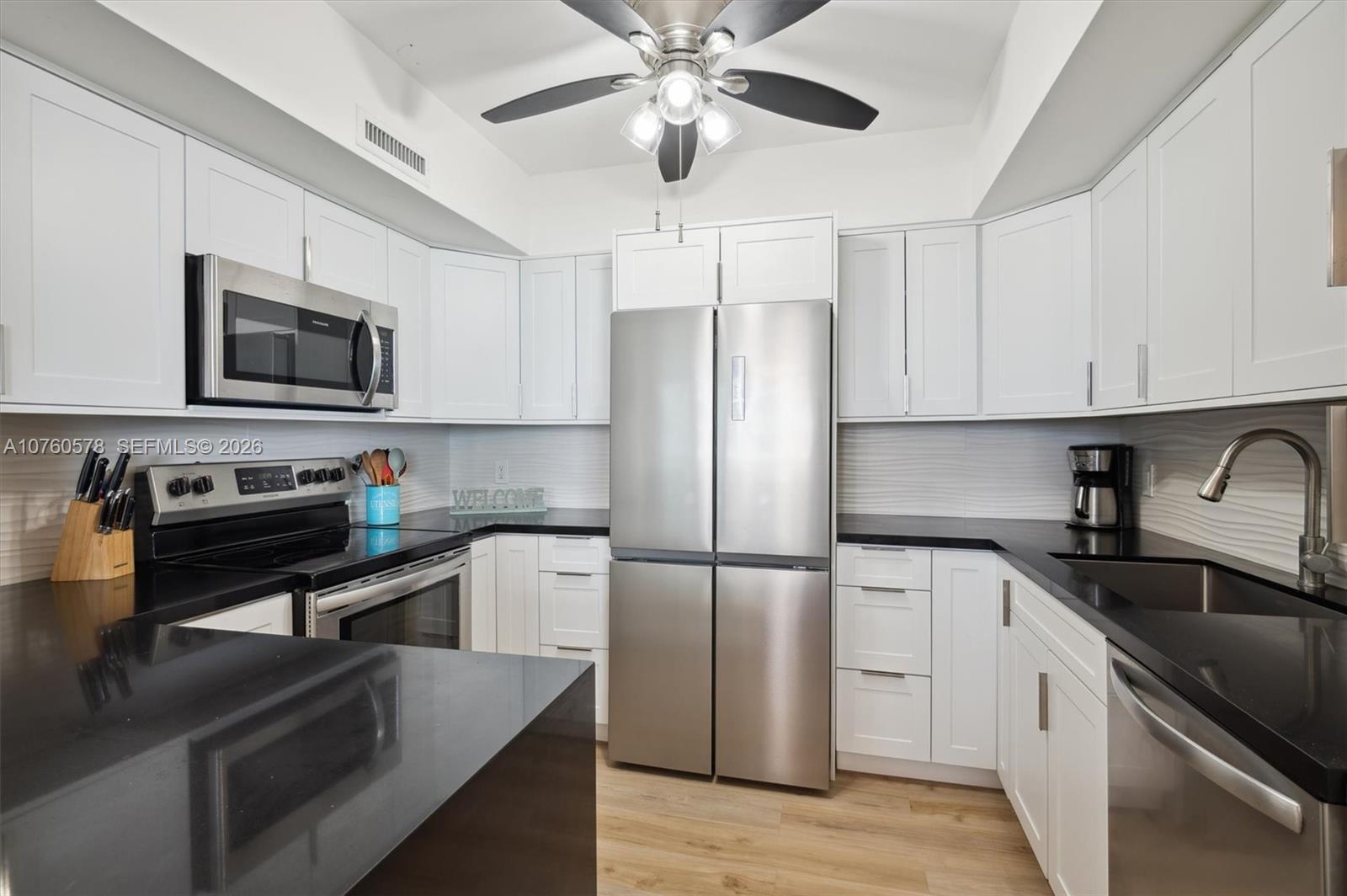 A kitchen features white cabinets, black countertops, stainless steel appliances, and a ceiling fan — 3505 S Ocean Dr # 710, Hollywood FL 33019, HOLLYWOOD, FL