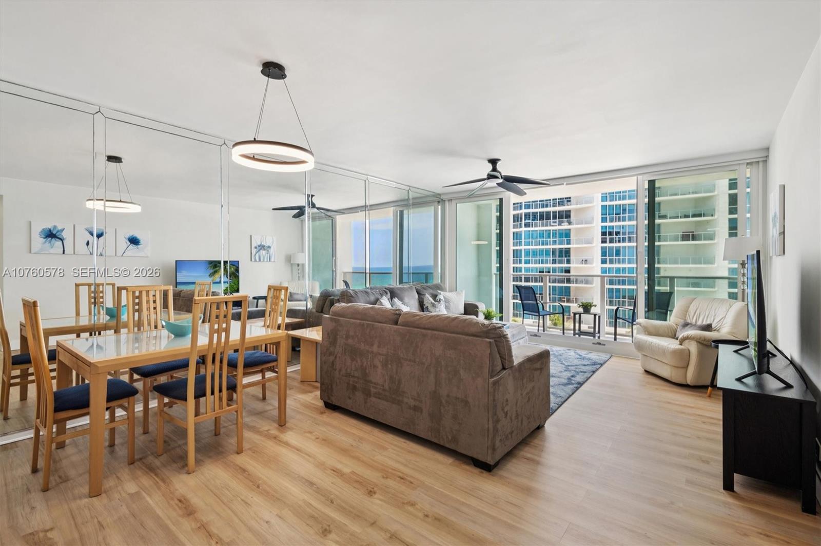 A living and dining area features light wood floors, mirrored walls, and a balcony view — 3505 S Ocean Dr # 710, Hollywood FL 33019, HOLLYWOOD, FL