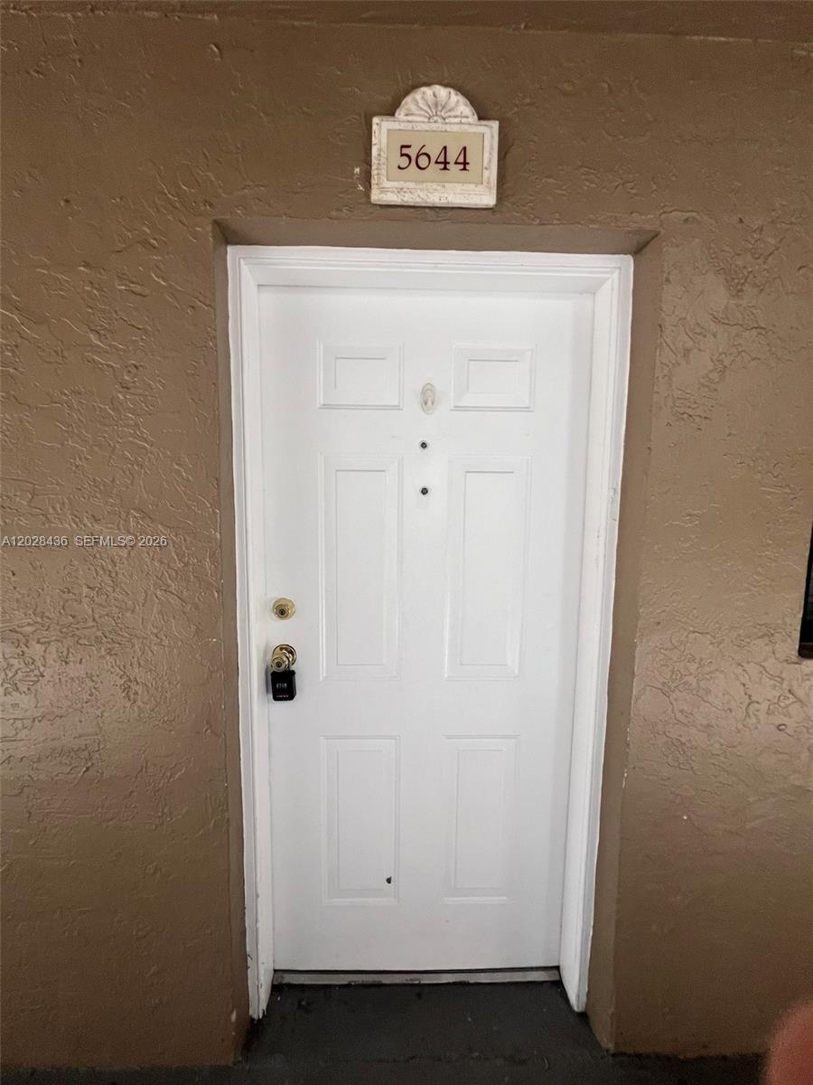 A white front door with a lockbox is set into a textured brown wall — 5644 W 25th Ct # 5644, Hialeah FL 33016, HIALEAH, FL