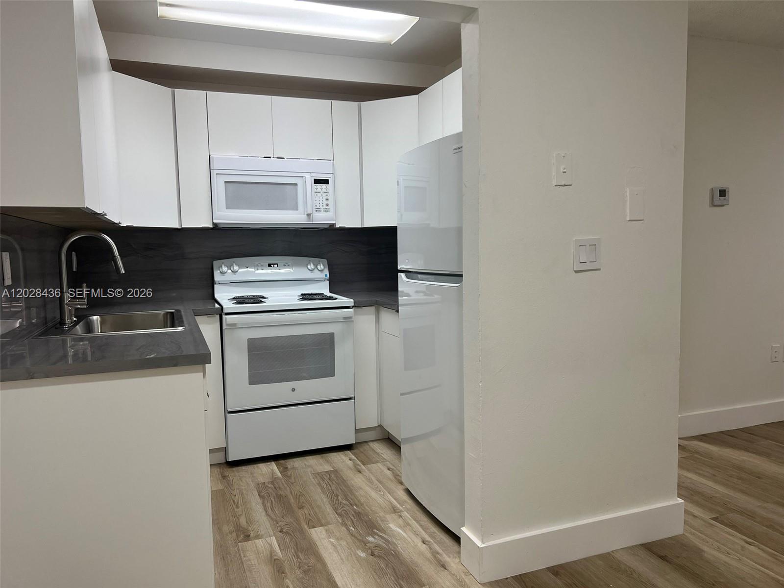 A kitchen features white cabinets, white appliances, dark countertops, and light wood-look flooring — 5644 W 25th Ct # 5644, Hialeah FL 33016, HIALEAH, FL